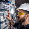 Male electrician at the checkout counter on a blurred background of a switchboard.