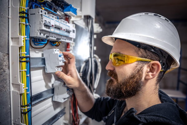 Male electrician at the checkout counter on a blurred background of a switchboard.
