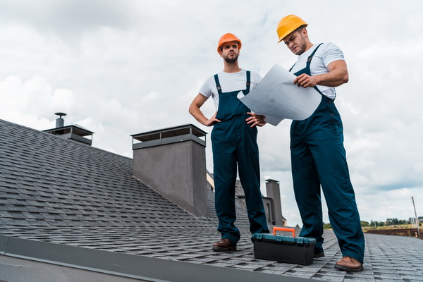 architect standing on roof with hands on hips near coworker with paper